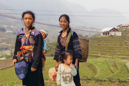 Sapa, Vietnam - April 15, 2016: Black Hmong minority woman carry child on the back while working and walking in the mountains. Traditional sling to carry kid on the backのeditorial素材