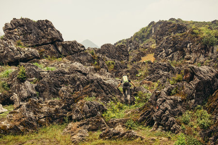 Man hiking with backpack high in the green mountains in summer. Landscape observation during a short break. Copy space on the clear sky in Vietnamの写真素材