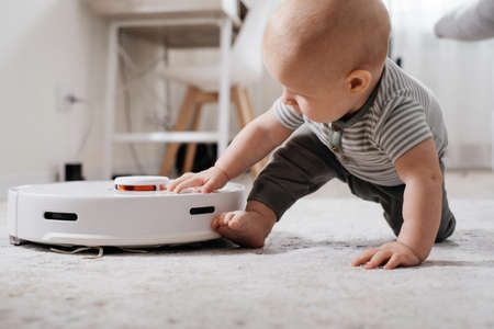 Baby on the floor with robot vacuum cleaner. Home appliances for family with kids that make life easier for mother. Carpet, rug autonomous tidying up, modern device for house with children.の写真素材