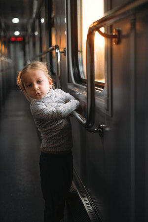 Toddler child looking though train window on sunset, bright sunlight, atmospheric travel by railway...