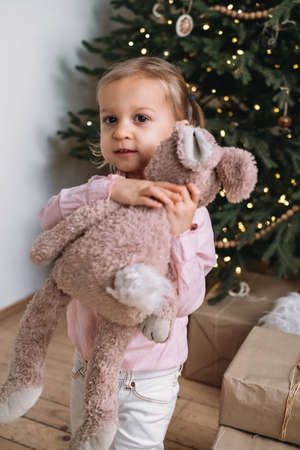 Happy child received Christmas present stuffed toy near tree at home. Kid getting gift in the morningの写真素材
