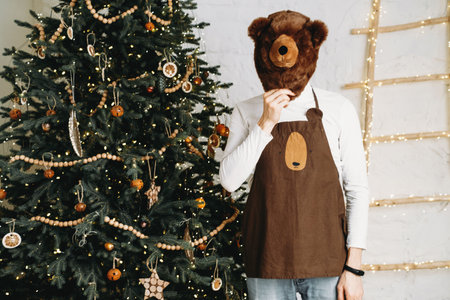 Funny man in front of Christmas tree ready for celebration with gifts in bear mask and costume. Surprise, carnival party for adultの写真素材