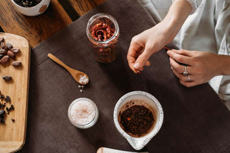 Woman hands putting chili pepper, solt in organic cacao, cooking on table, cocoa nibs, beans, artisanal chocolate making in rustic style for ceremony. Chocolate making with pounder close-up top viewの写真素材