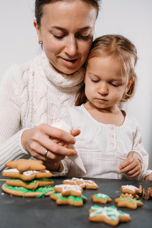 Mother with child decorating gingerbread cookies with icing for Christmas. Homemade festive food. Cute toddler girl Family Workshop. Stars, treeの写真素材