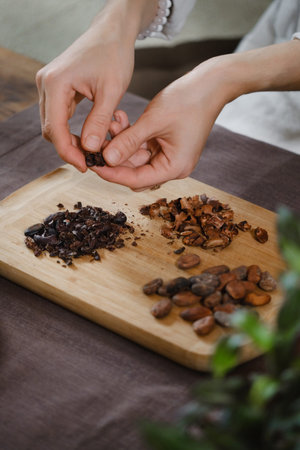 Hands peeling organic cacao beans on wooden table, cocoa nibs, artisanal chocolate making in rustic...