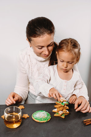 Mother with child decorating gingerbread cookies with icing for Christmas. Homemade festive food. Cute toddler girl Family Workshop. Stars, treeの写真素材