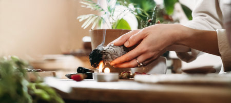 Woman hands burning white sage, palo santo before ritual on the table with candles and green plants. Smoke of smudging treats pain and stress, clear negative energyの写真素材