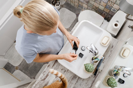 Man cleaning electronic shaving razor in sink, male self care and personal hygiene Top view. Hair in sink with cat. Long blonde hair, machine in handsの写真素材