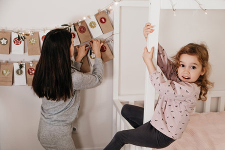 Mother with child opening Christmas advent calendar tasks and gifts. Toddler girl excited about festive surprise in craft bag at home. Family celebration and preparation for New Yearの写真素材