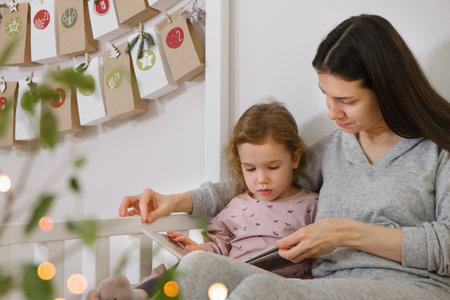 Mather with toddler child reading book or photo album on Christmas eve near eco advent calendar in kids room on the bed. Night story for girl with family. happy festive time memories together.の写真素材