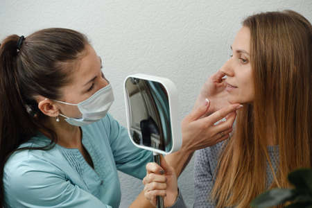 Client checking with dermatology cosmetician specialist with mirror, discussion skin face problems and therapy methods, results. Woman showing zones for treatment. beautician with customerの写真素材