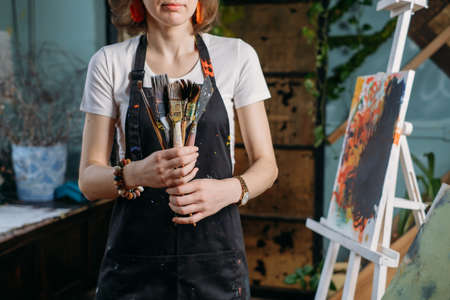 Painter working in real studio with oil paints and brushes, creating canvas, modern art. Young woman over window, closeupの写真素材