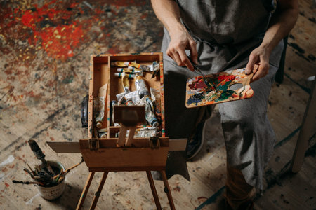 Painter working in real studio with oil paints and brushes, creating canvas, modern art. Young man...