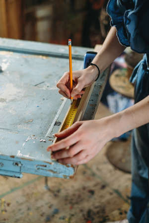 Close up view of hardworking professional carpenter woman hands working with ruler, making marks on wood. Reuse, reduce, recycle old things. Aware consumption and gender equality. Tools to repairの写真素材