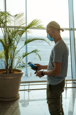 Man with power bank at the airport, charging phone to stay connected during travel, before flight at...