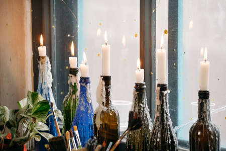 Candles in colorful bottles. melted wax, by the window. Natural light, creative atmosphere vintage look on windowsillの写真素材