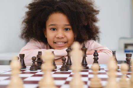 African American girl playing chess. Happy smiling child behind chess smiling in class or school lesson. Excited clever black kid with board game close-upの写真素材