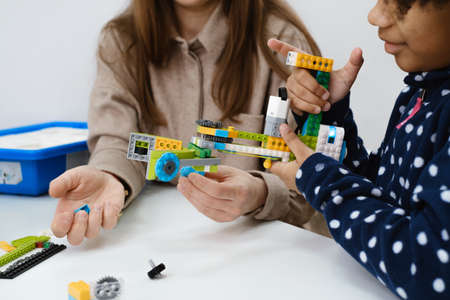 Multiethnic kids at STEM lesson constructing robot in classroom with woman teacher Children making electronic arm model at modern science school African American, Caucasian pupils learning technologyの写真素材