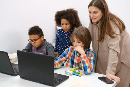 Multiethnic kids at STEM lesson constructing robot in classroom with woman teacher Children making...
