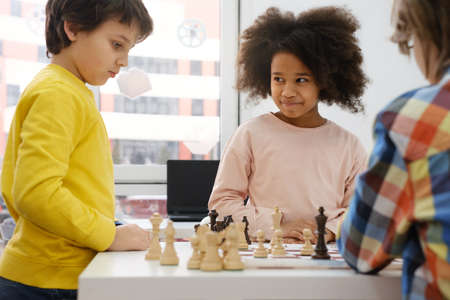 Diverse Group of kids playing chess. Concentrated multiethnic clever children with board game having fun at school. African American girl and Caucasian boys on chess lesson strategyの写真素材