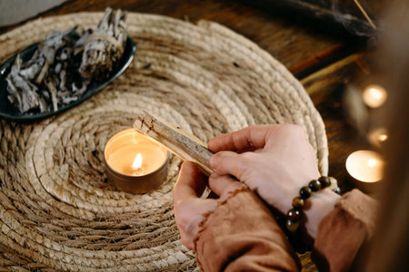 Woman hands burning Palo Santo, before ritual on the table with candles and green plants. Smoke of...