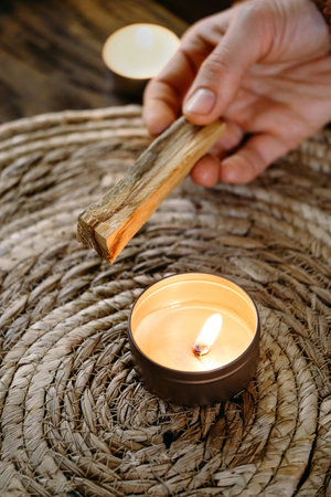 Woman hands burning Palo Santo, before ritual on the table with candles and green plants. Smoke of smudging treats pain and stress, clears negative energy and meditation wooden stickの写真素材