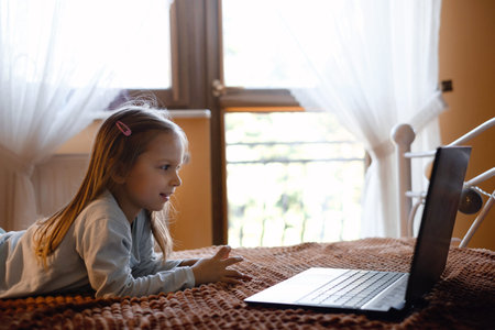 Child watching cartoons on laptop. Serious kid with technology at home on bed spending time on-line....