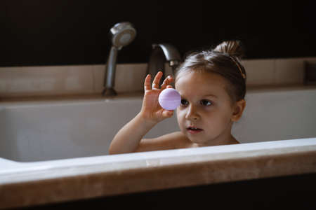Child holding bath bomb. Relaxing hygiene procedure for kids. Aromatherapy and fun at home. Happy toddler girl in bathtub washing herselfの写真素材
