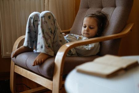 Bored sad toddler child lonely at home sitting on armchair. Sad relaxed candid kid at home in cozy warm atmosphere. Girl thinking, dreaming. Copy spaceの写真素材