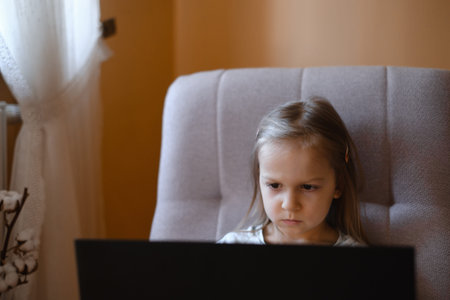 Child watching cartoons on laptop. Serious kid with technology at home in armchair spending time...