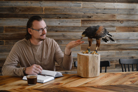 Man is working, writing with wild bird at home by the table. Making noted, memories, diary with...