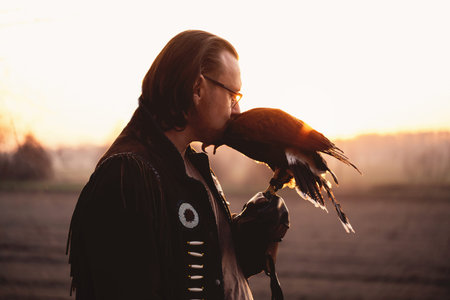 Man and wild bird over sunset sky looking on each other Buzzard or eagle symbol of power, victory, courage, greatness and spiritual uplift, brave person in eye glasses, vision problemsの写真素材