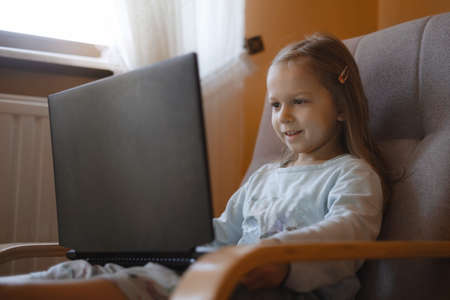 Child watching cartoons on laptop. Serious kid with technology at home in armchair spending time on-line. Education and entertainment for toddlers. Girl in cozy atmospheric roomの写真素材