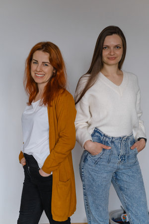 Happy two women in their 20s 40s over white wall. Employees in casual outfit looking at the camera....