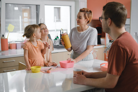 Happy family with kids cooking on modern kitchen. Children cutting fruit salad, preparing food with...