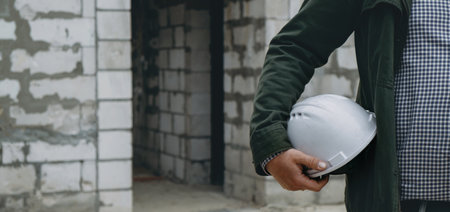 Construction Worker at Site holding helmet close-up. Smart civil architect engineer inspecting and working outdoors building sideの写真素材