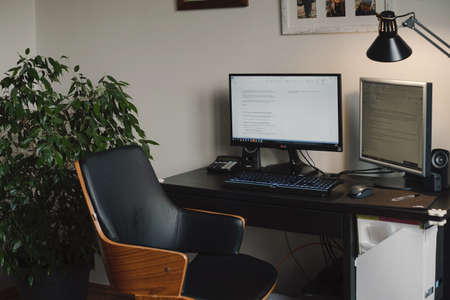 Freelancer workspace, home working place with computer and screen. Comfortable desk without people with home plant and lamp. Boho vintage chair by the windowの写真素材
