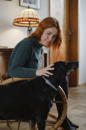 Woman on rocking chair stroking big black dog. Relaxed home atmosphere. Vintage house for slow living. Female at her 40s having rest.の写真素材