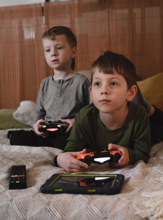 Kids playing video games at home on the bed at night. Boys using game console and having fun in the evening. Brothers using technologies exited. Boy with remote controlの写真素材