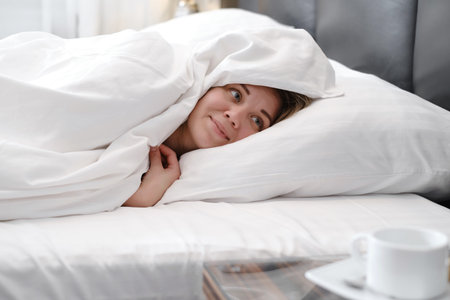 Woman covered with blanket in the morning in bed. Woman waking up from sleep in the morning. woman...