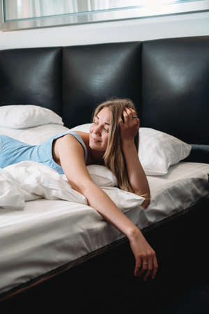 Attractive woman in hotel room lie in bed, Passionate Female in bodysuit having rest in modern hotel while traveling. Sunny morning in bedの写真素材