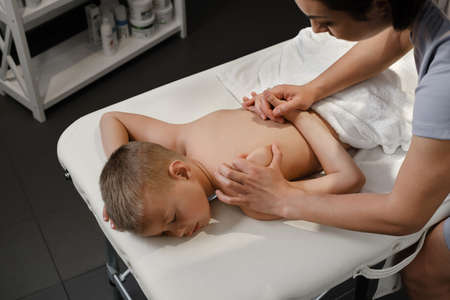 masseur gives the child a back massage. Kids massage concept. massage therapist giving 7 year old boy shoulder massage. Physical therapyの写真素材