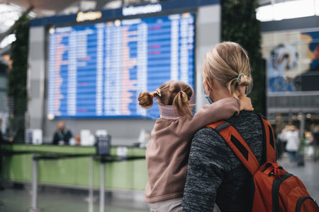 Man and girl watching timetable information at the airport, passengers waiting for a plane. Family...