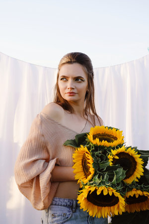 Romantic woman with sunflowers over white fabric background outdoors. Clean skin and natural beauty. Rural summer vacationの写真素材