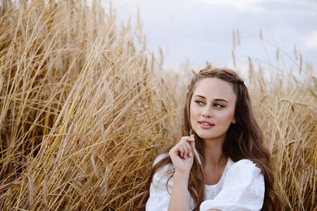Beautiful woman on wheat field. Young female with makeup beauty portrait outdoors. Ukrainian agricultural land with rye. Boho chic style.の写真素材