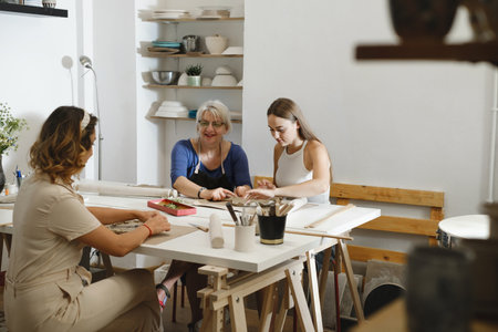 Pottery workshop in studio. People working with clay on the table. Adults learning to do ceramic plates. Pottery as hobby and leisure activityの写真素材