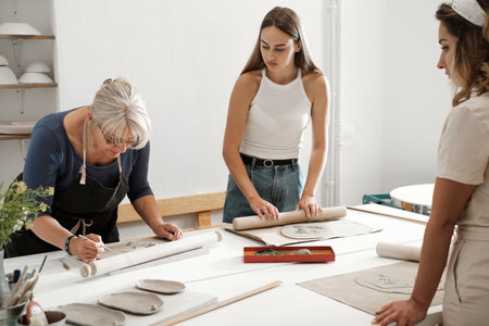 Pottery workshop in studio. People working with clay on the table. Adults learning to do ceramic plates. Pottery as hobby and leisure activityの写真素材