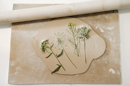 Clay handmade Ceramic plates, rolled clay on the table with plants and flowers. Top view on...