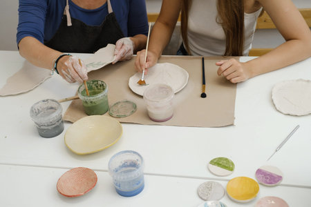 Top view potter hands with paintbrush glazing, painting on plate in workshop, working in pottery...