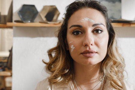Close-up dirty woman potter portrait, self-employed pottery artist in creative studio working with...